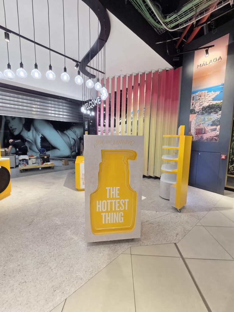 Instalación retail de Sol de Janeiro en el aeropuerto de Málaga, con diseño tropical, estructura amarilla The Hottest Thing y ambientación experiencial.